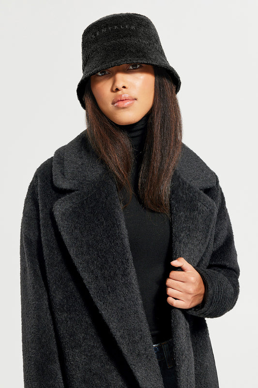 Sentaler Bouclé Alpaca Bucket Hat and Bouclé Alpaca Mid Length Oversized Notched Collar Coat featured in Bouclé Alpaca and available in Black. Seen from front close up on model.