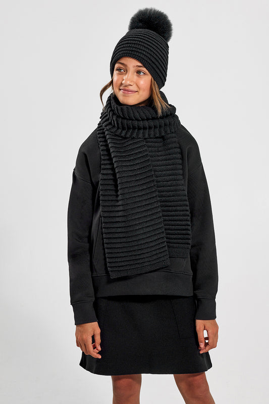 Sentaler Kids (6-14 Years) Ribbed Hat with Oversized Fur Pompon and Ribbed Scarf featured in Baby Alpaca and available in Black. Seen from front above the knees on model.